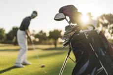 Image of golf clubs with a man swinging a golf club in the background,