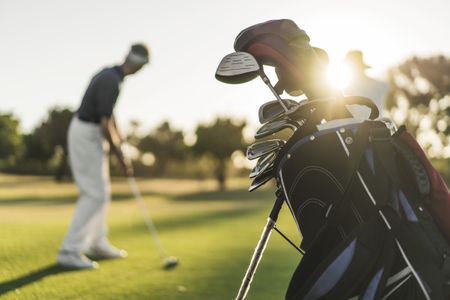 Image of golf clubs with a man swinging a golf club in the background,