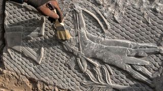 A worker brushes a rock-carving relief found in Iraq of an ancient warrior.