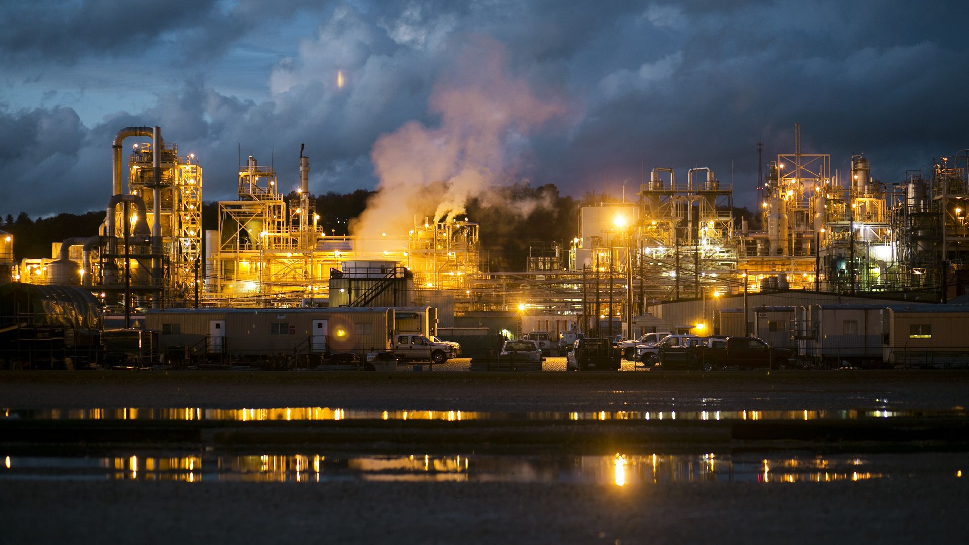 A chemical works at night, with steam illuminated by orange light.