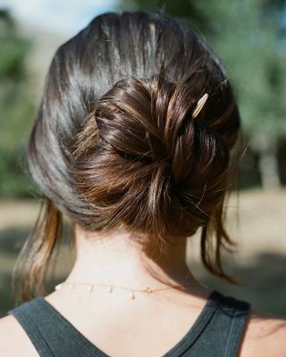 A young woman is captured from behind as she wears a black top, a golden necklace with tiny pendants, and a hair stick in silver.