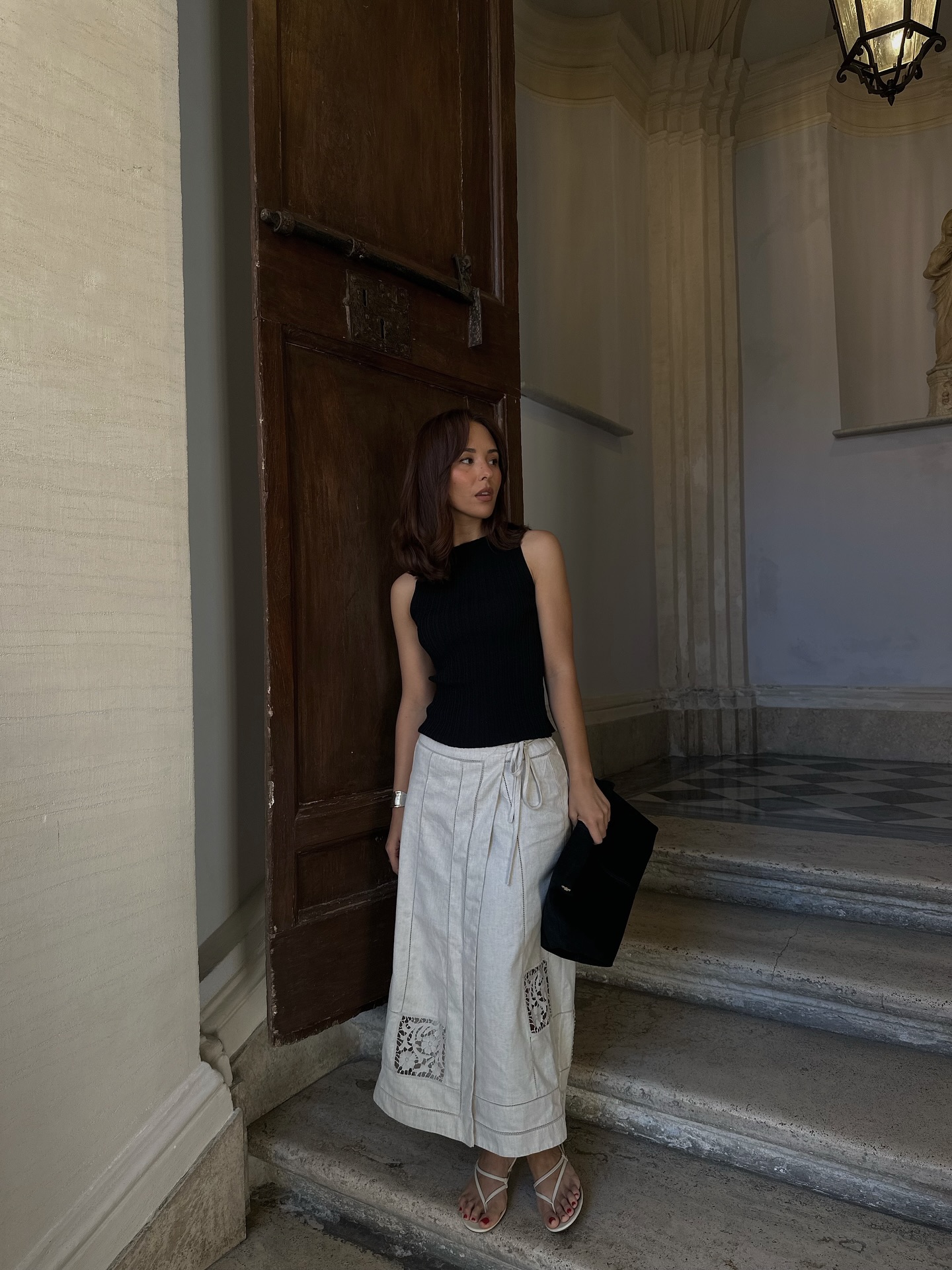 An image of @deborabrosa wearing one of the best linen skirts with strappy what sandals and a black tank.