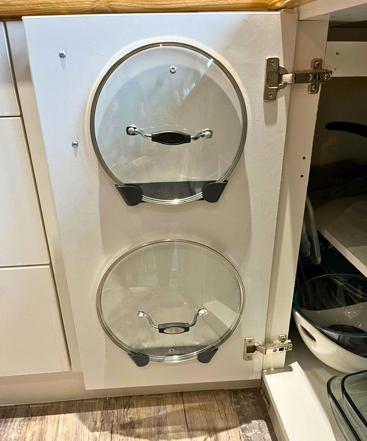 Two glass pan lids held on the inside of my kitchen cabinet door in the nifty adhesive Joseph Joseph pan lid holders