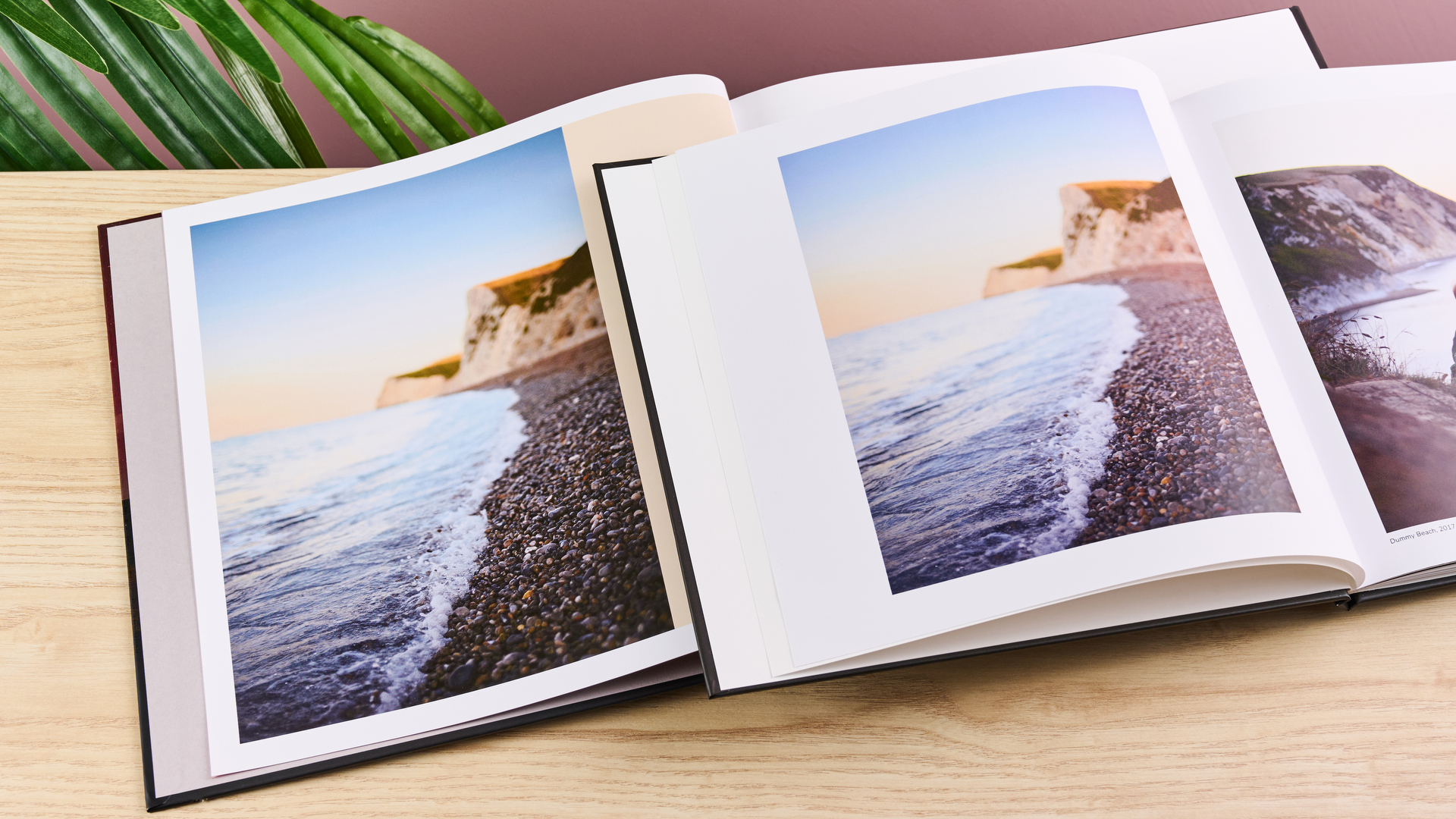 The Once Upon photo book sits on top of the Blurb photo book. Both pages show a two-page spread of the same image of a pebble beach and cliffs.