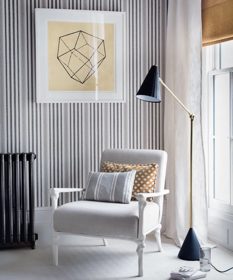 bedroom with monochrome stripe wallpaper, white armchair, black floor lamp and yellow blind