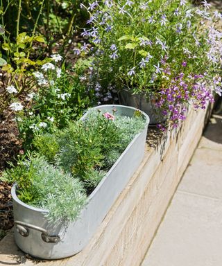 Timbered raised garden bed with metal herb pots on the edge.