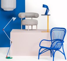 A selection of furniture in a studio, including a blue wicker chair, a angle-poise lamp and a boucle accent chair