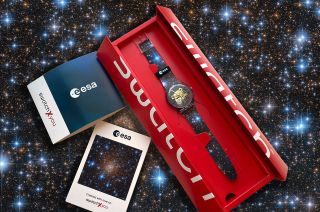 photo of a wristwatch inside a small red case, with a photo of distant stars in the background.