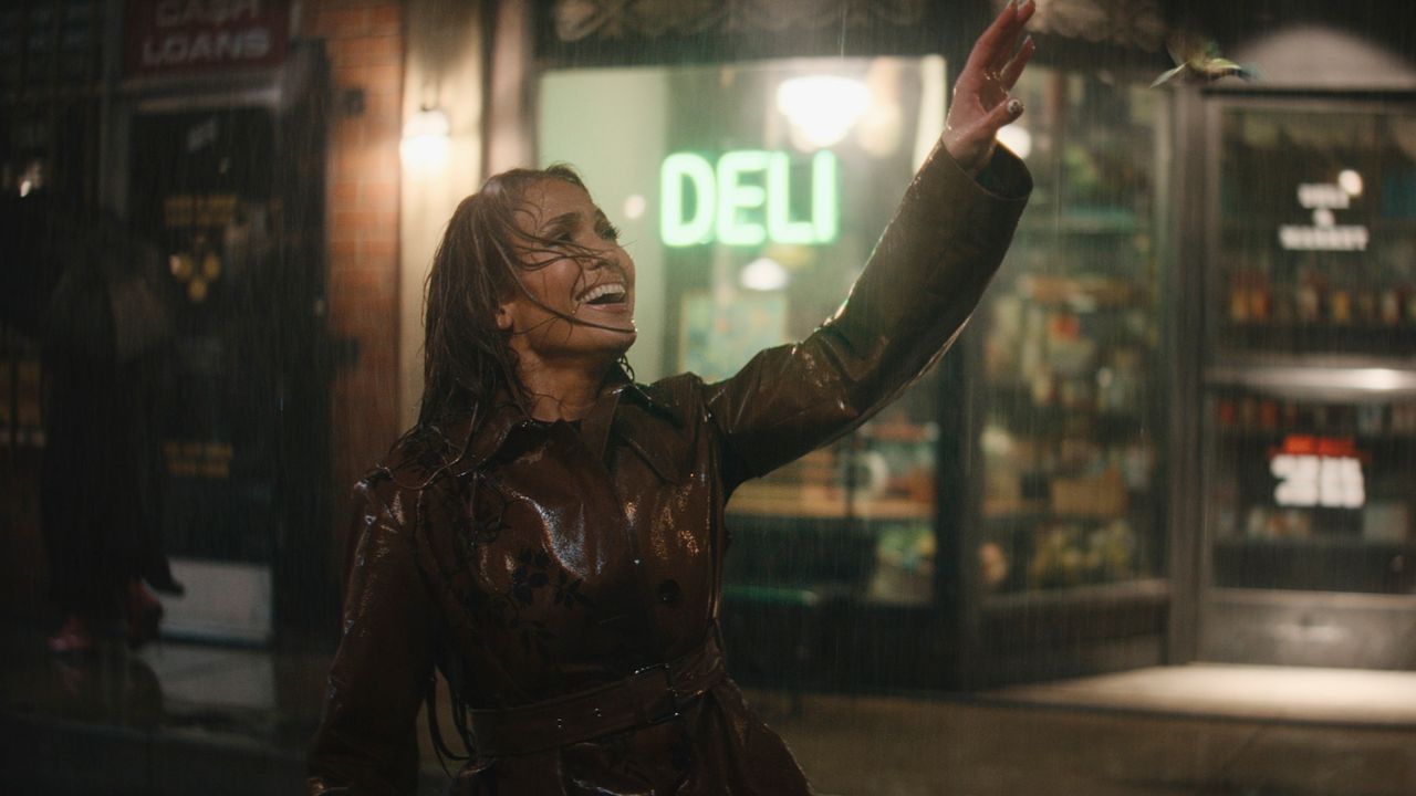 a woman (jennifer lopez) raises her arm while singing in the rain