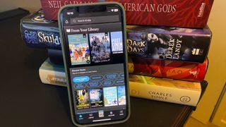 The Kindle app open on an iPhone while placed in front of a pile of books.