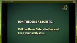 A CRT-style screen showing a media player, playing a video stopped on a frame reading "Don't become a statistic, call the Home Safety Hotline and keep your family safe."