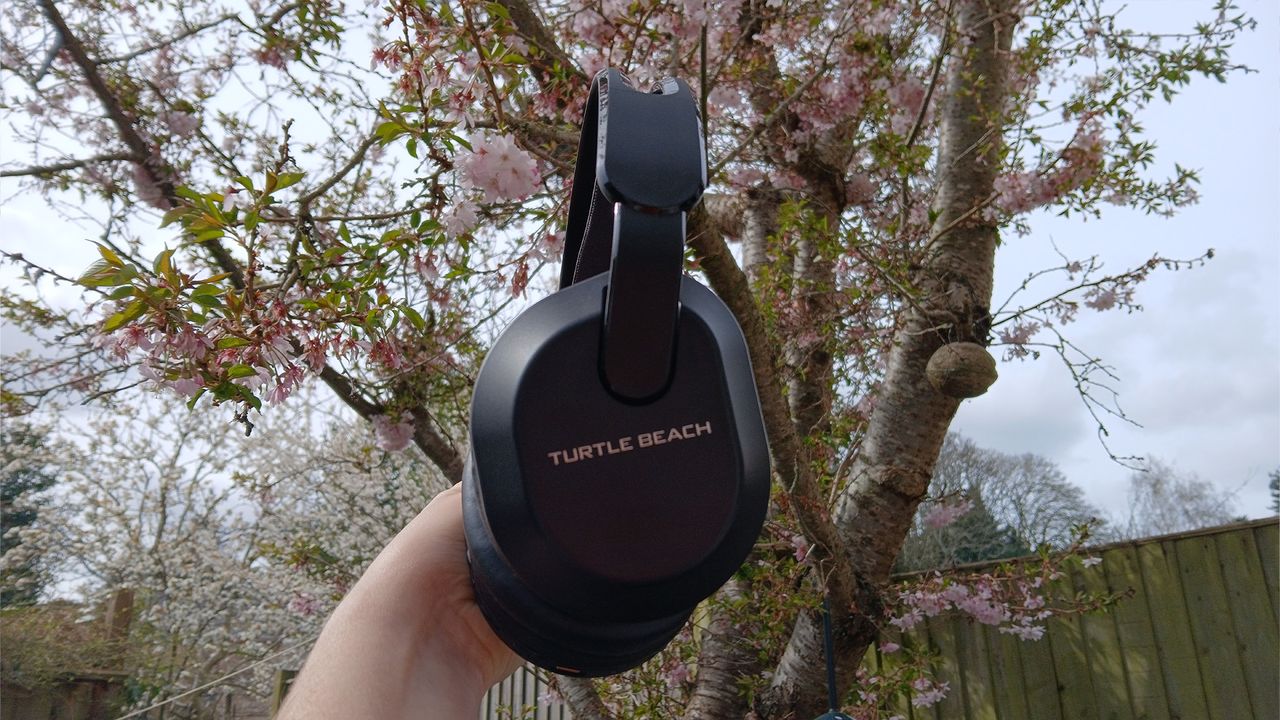A Turtle Beach Stealth 500 headset in the black colourway, held up outdoors with a tree in the background.