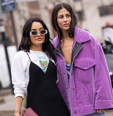 PARIS, FRANCE - MARCH 04: Amina Muaddi wearing a printed t-shirt, black dress, burgundy Loewe bag and Gilda Ambrosio wearing a purple midi dress, purple jacket and green Loewe bag, are seen outside Loewe, during Paris Fashion Week - Womenswear F/W 2022-2023 on March 04, 2022 in Paris, France. (Photo by Claudio Lavenia/Getty Images)