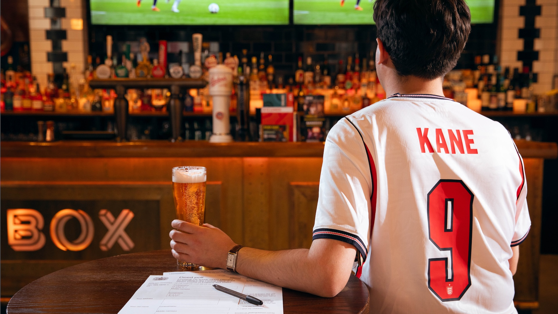 Man wearing a Harry Kane shirt watching the football with a pint 