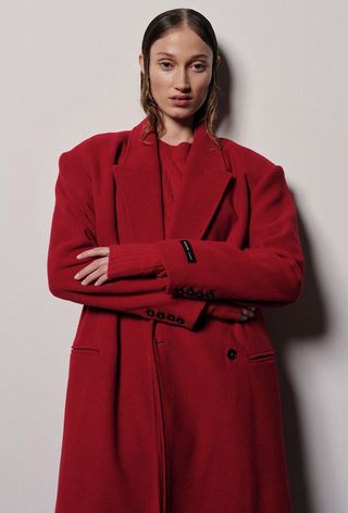 One of the best jacket coat brands, Herskind, is shown in an image of a model wearing a red coat over a red crewneck sweater