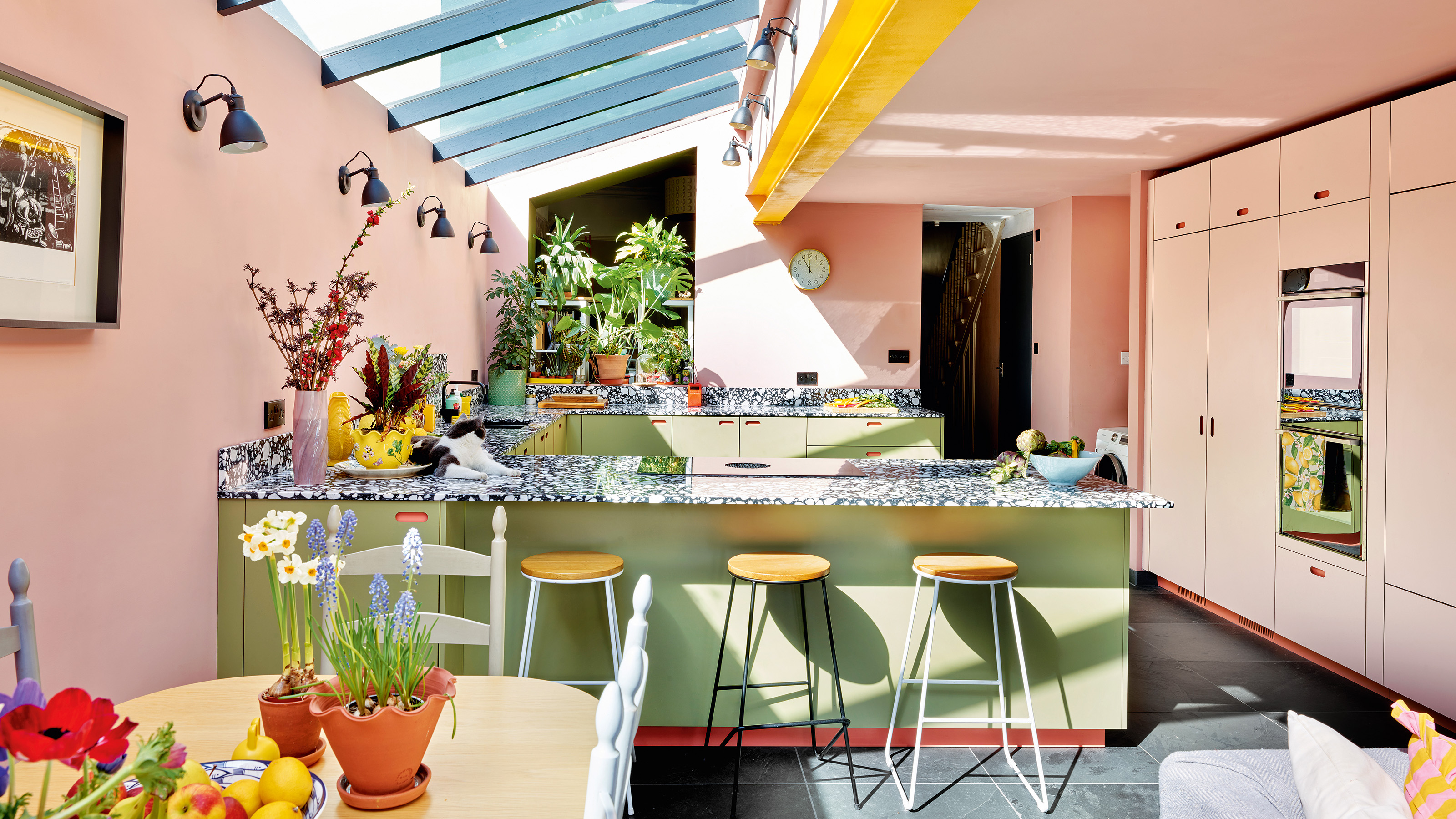 colourful kitchen with side extension pink ceiling yellow steel beams and U-shaped kitchen with green cabinets and black and white worktop and a full height pink pantry