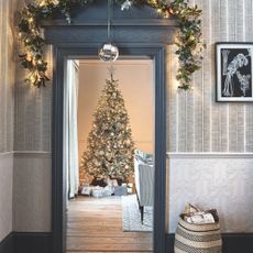 Decorated Christmas tree with presents below, through a grey ornate doorway that has a matching wreath above it