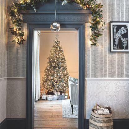 Decorated Christmas tree with presents below, through a grey ornate doorway that has a matching wreath above it