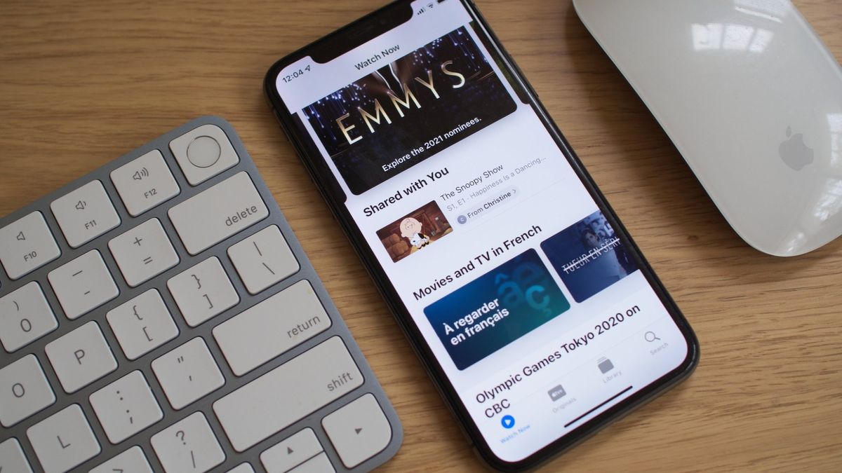 An iPhone between a keyboard and mouse, with the Apple TV app open