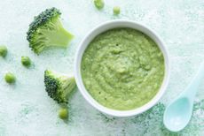 Broccoli purée on a blue table with pieces of broccoli surrounding