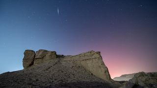 a streak of light crosses the night sky above the desert
