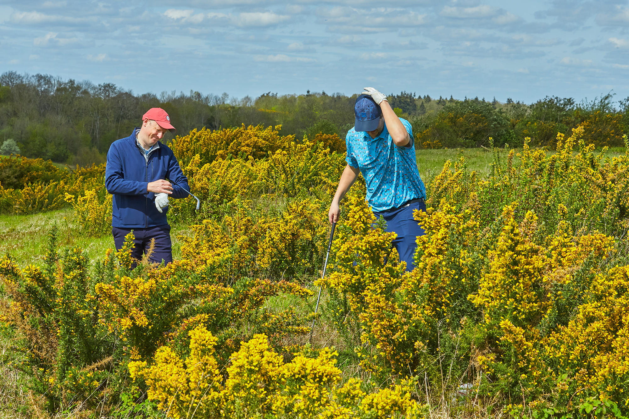 Two golfers searching for a lost golf ball, with one indicating that the search has gone on for too long and is impacting pace of play negatively