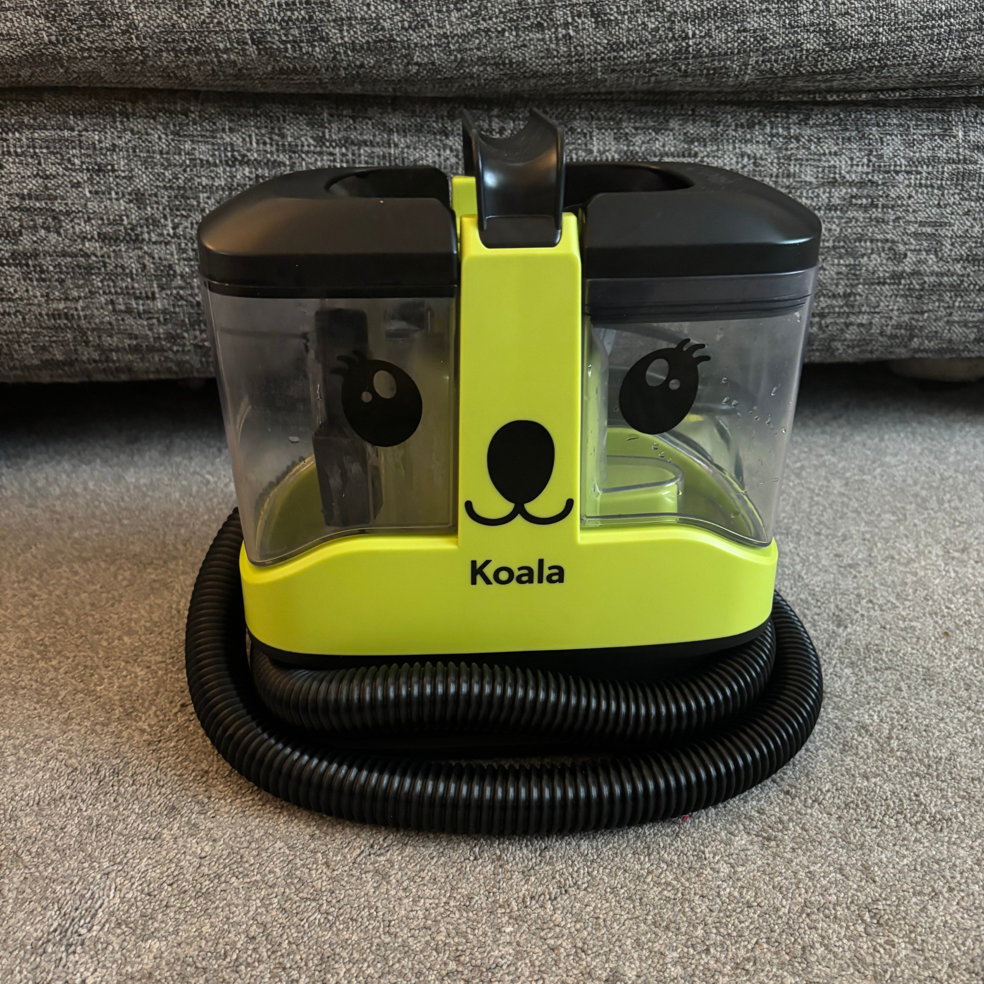 Front view of the Gtech Koala Spot Cleaner on grey carpet in front of sofa