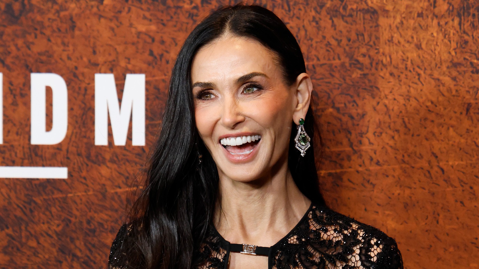 a woman with long dark hair posing in front of an orange backdrop