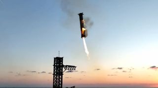 a cylindrical silver rocket comes down for a landing next to its launch tower with the ocean in the background