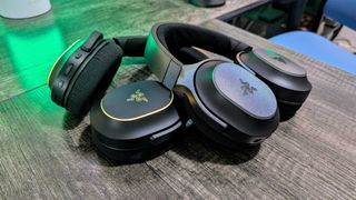 Two Razer Barracuda X Chroma headsets leaning against each other on a desk with a green backlight.