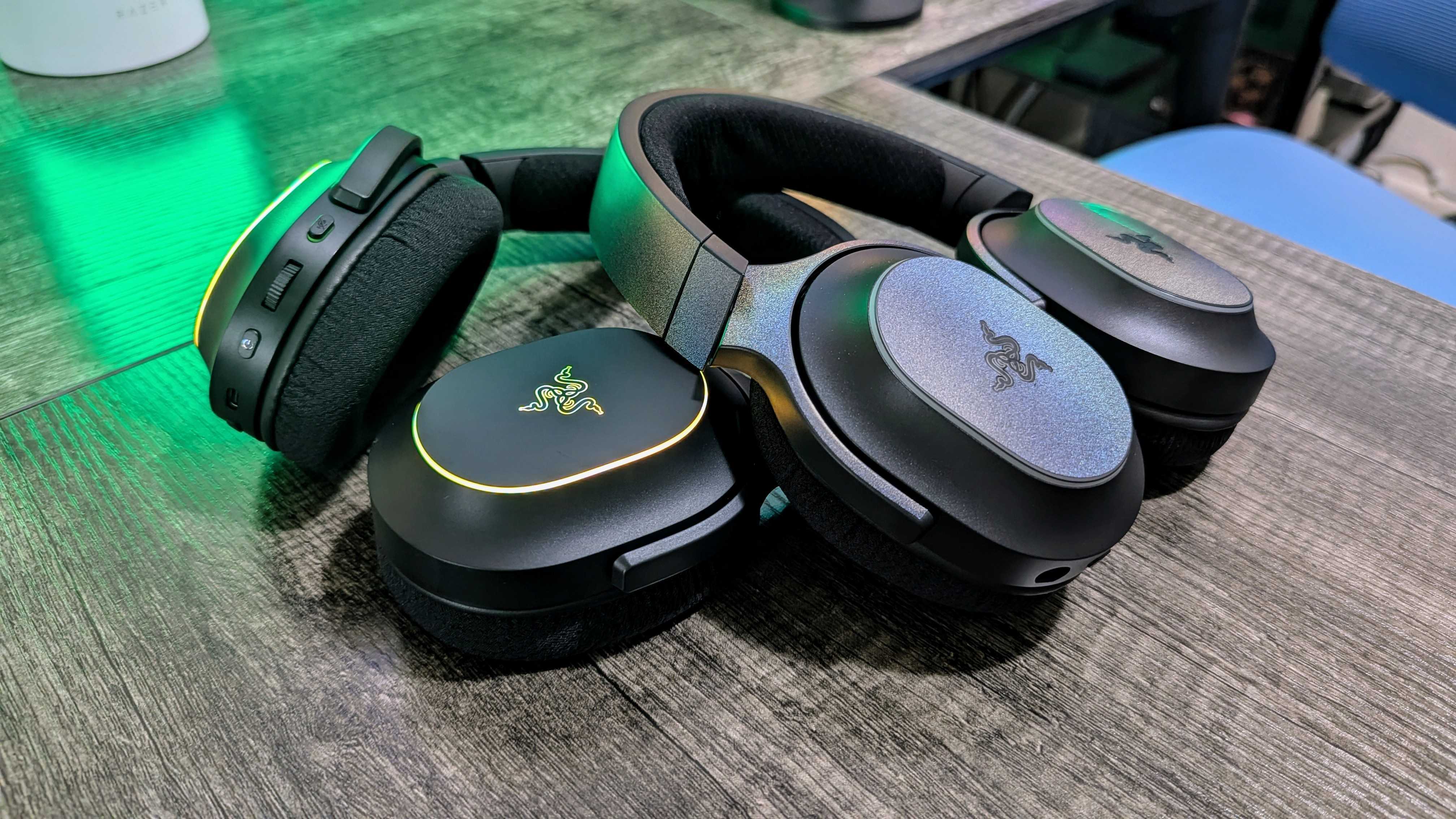 Two Razer Barracuda X Chroma headsets leaning against each other on a desk with a green backlight.