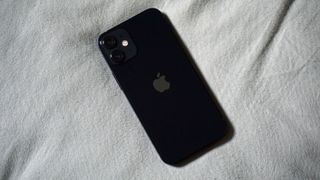 En svart iPhone 12 Mini ligger på ett vitt lakan med baksidan vänd uppåt.