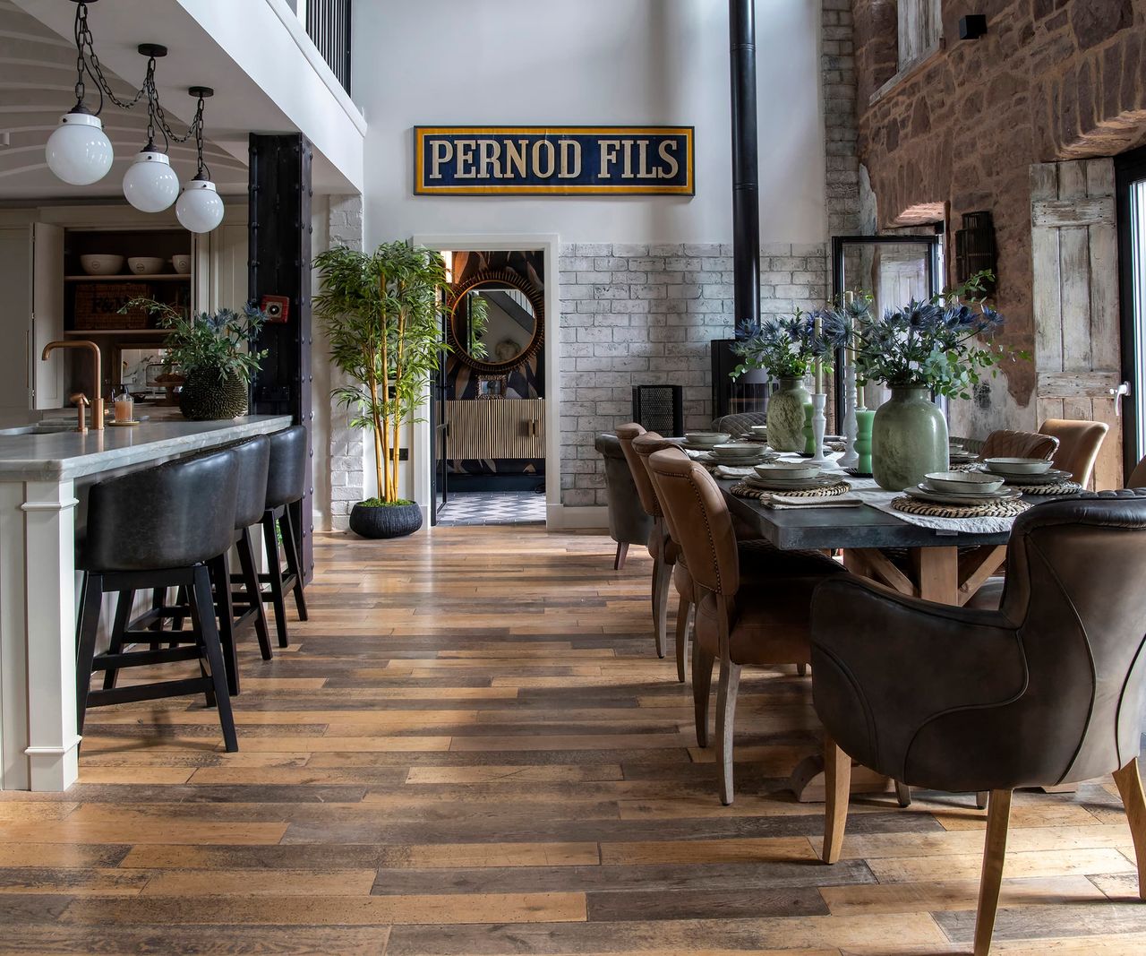 A kitchen-diner with a long dining green table with a brick wall facing the table
