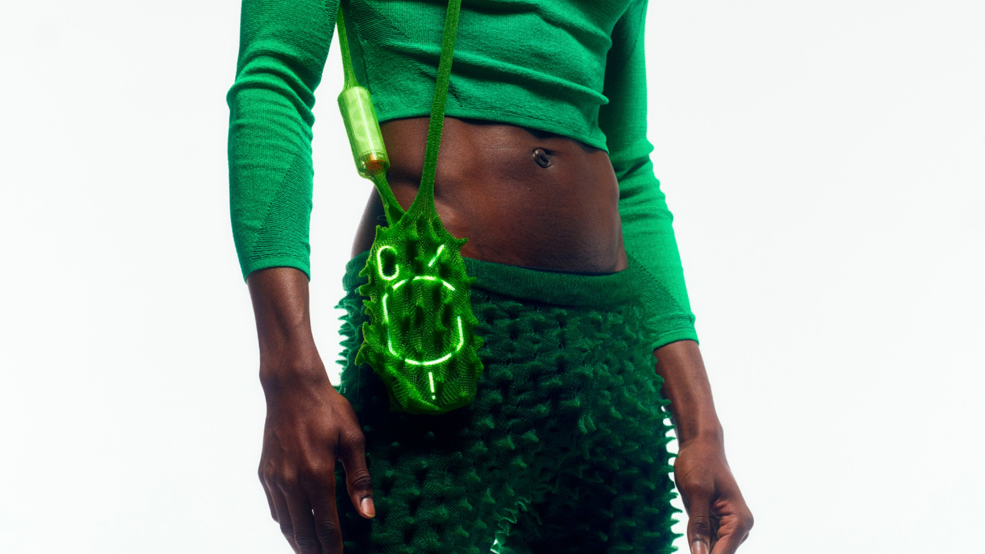 Nothing Ear (stick) worn inside a green bag, slung across the shoulder of a model, on white background