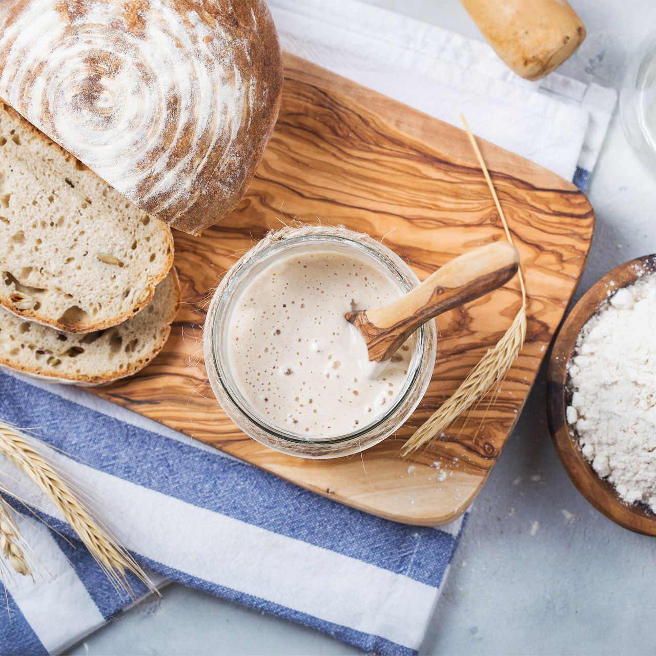 Sourdough starter next to loaf of bread and flour