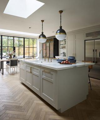 An example of how to plan kitchen lighting with pendant lights over a grey kitchen island with large windows, a skylight and herringbone wood flooring.