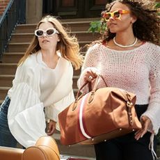 Two women wearing Saks Fifth Avenue clothing lifting a bag into a convertible car