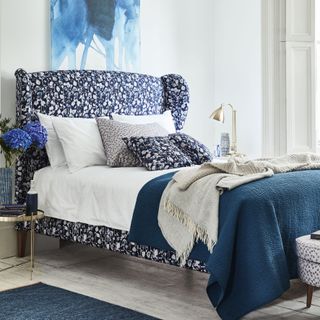 bedroom with white wall blue designed bed with cushions frame and wooden flooring