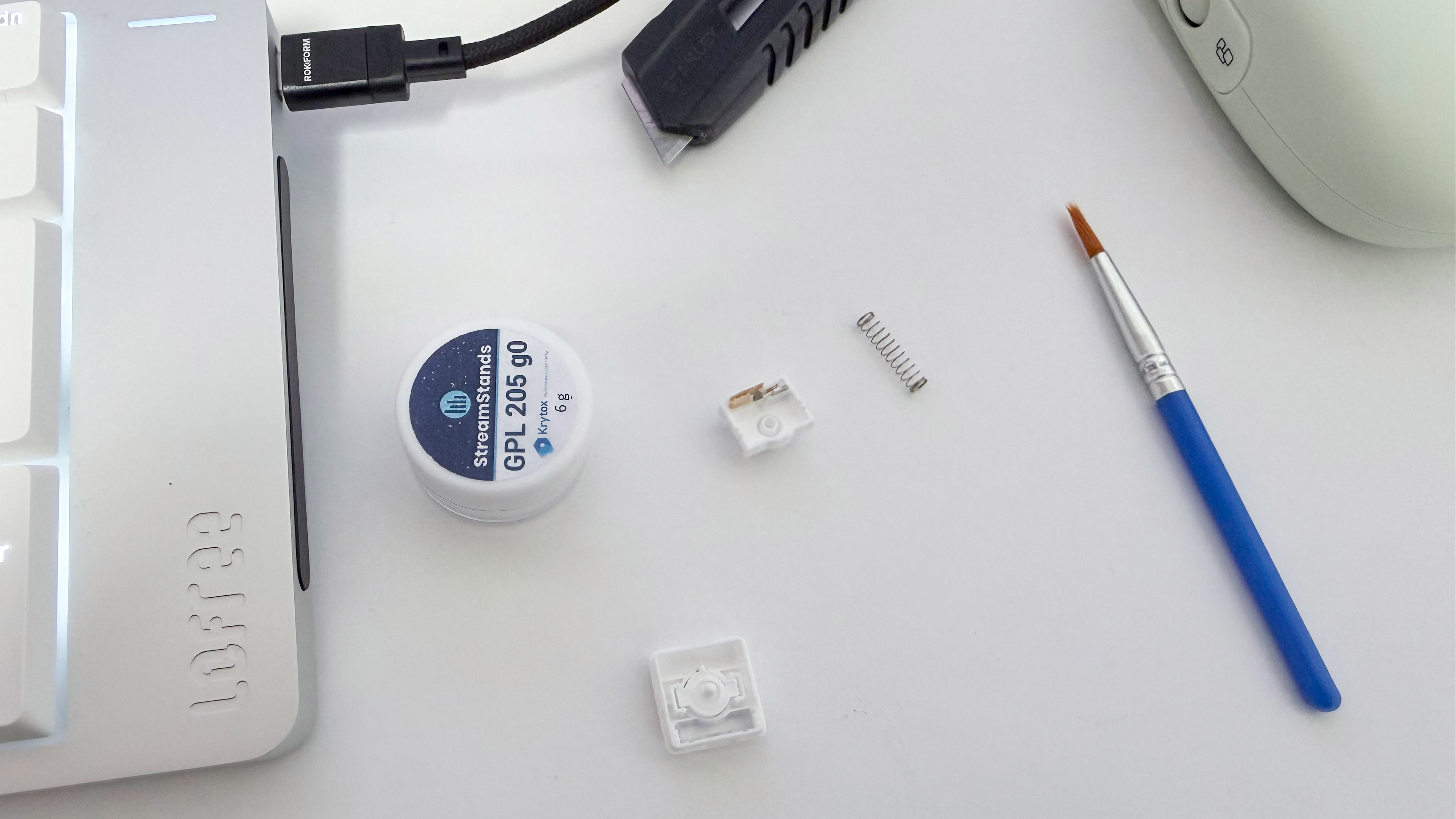 A photo of a Lofree Flow 2 switch having been taken apart, with some keyboard switch lube and an application brush.