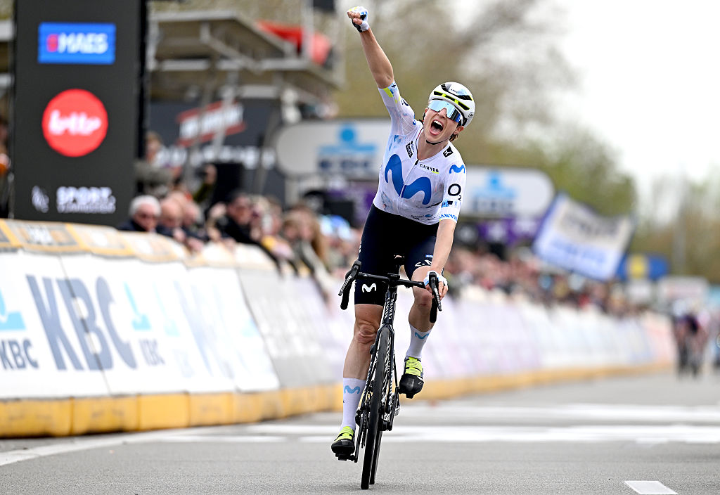 Marlen Reusser wearing a white jersey with blue M for Movistar celebrates with one arm raised