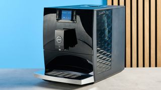 the jura c8 automatic coffee machine in piano black photographed with a blue and wood background
