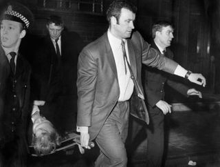 Rangers coach Jock Wallace, second right, helps stretcher-bearers to carry a man out of Ibrox after the disaster