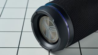 a black portable bluetooth speaker with LED panels sits atop a white table with a blue background