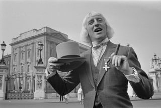 Jimmy Savile posing with his OBE at Buckingham Palace in 1972