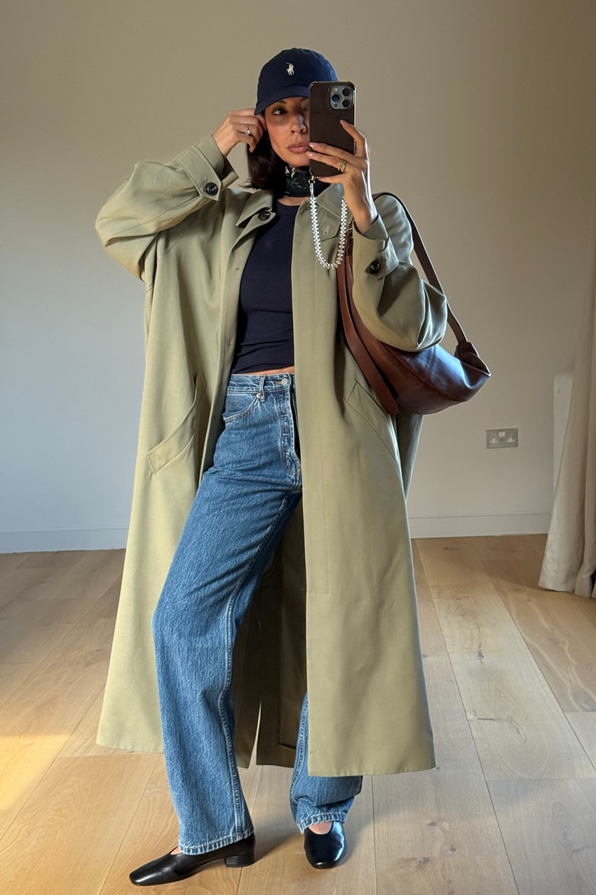 a woman wearing a baseball cap, trench coat, black t-shirt, straight-leg jeans, and black flats