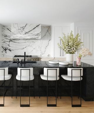 kitchen countertop trends, black and white kitchen with large black kitchen island with sink and seating, marble backsplash and cooker hood, white custom cabinetry