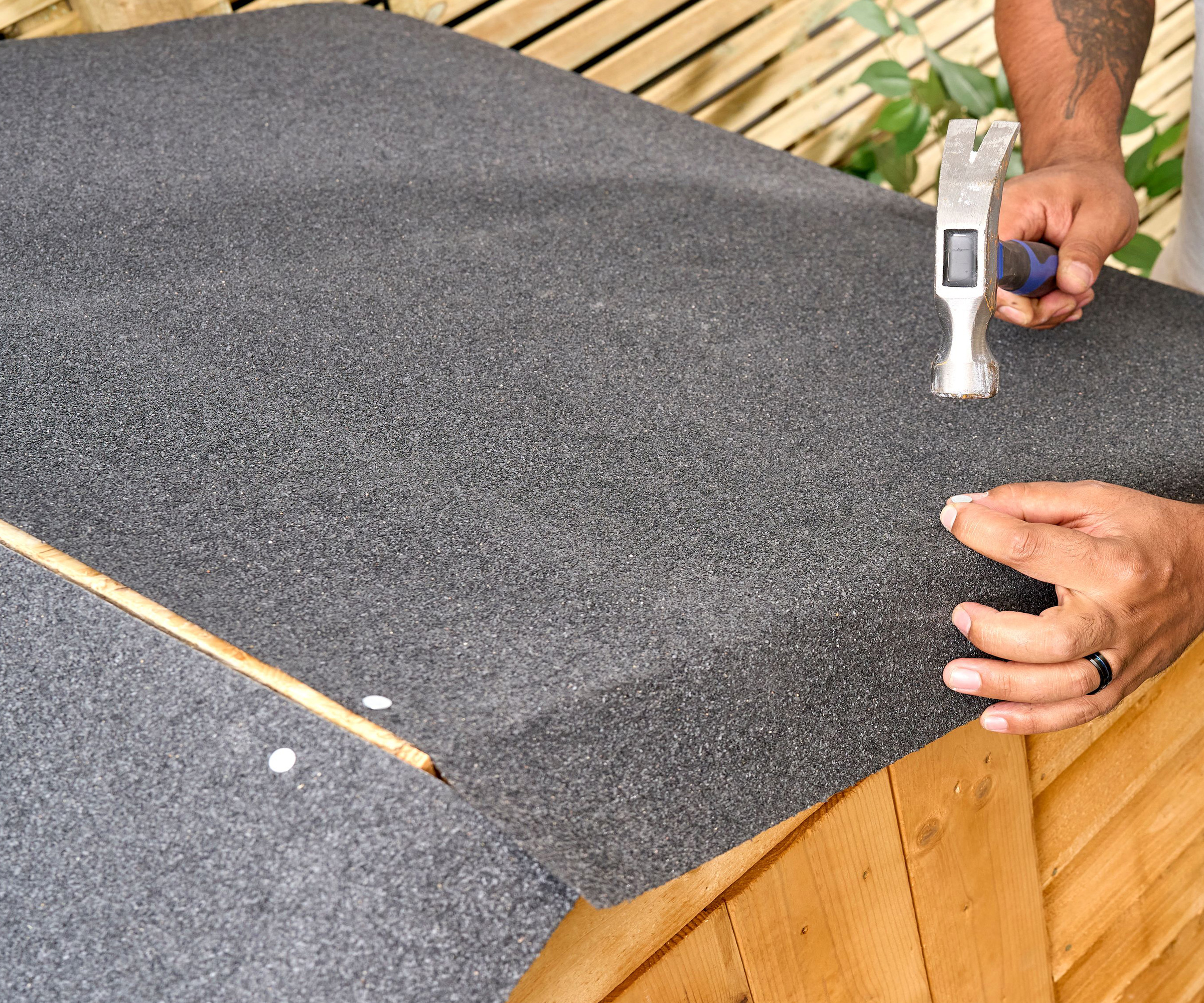 Nails pinning down grey shed roof felt with a hammer