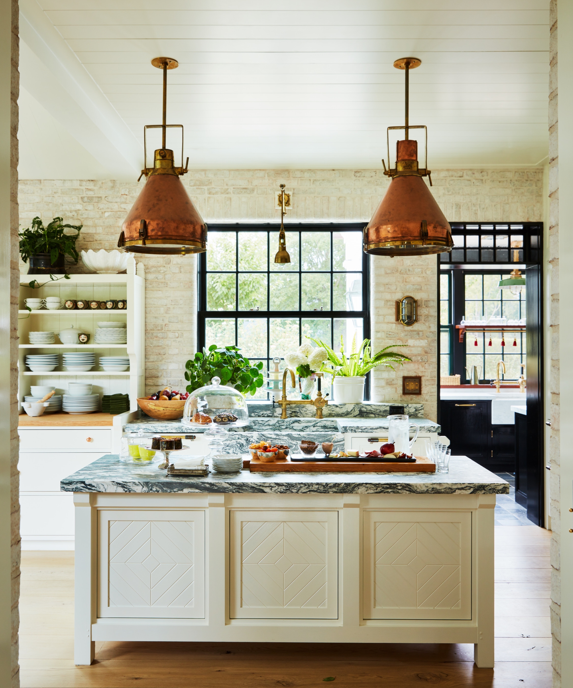 A neutral country kitchen with warm white cabinets, dramatic marble countertops and a mix of storage styles for maximum function
