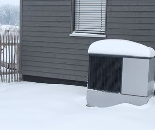 Heat pump in front of house wall in winter in the snow