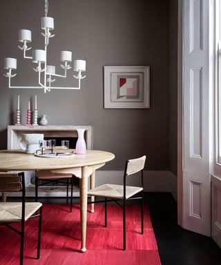 grey dining room with round table, sculptural statement pendant light and red rug